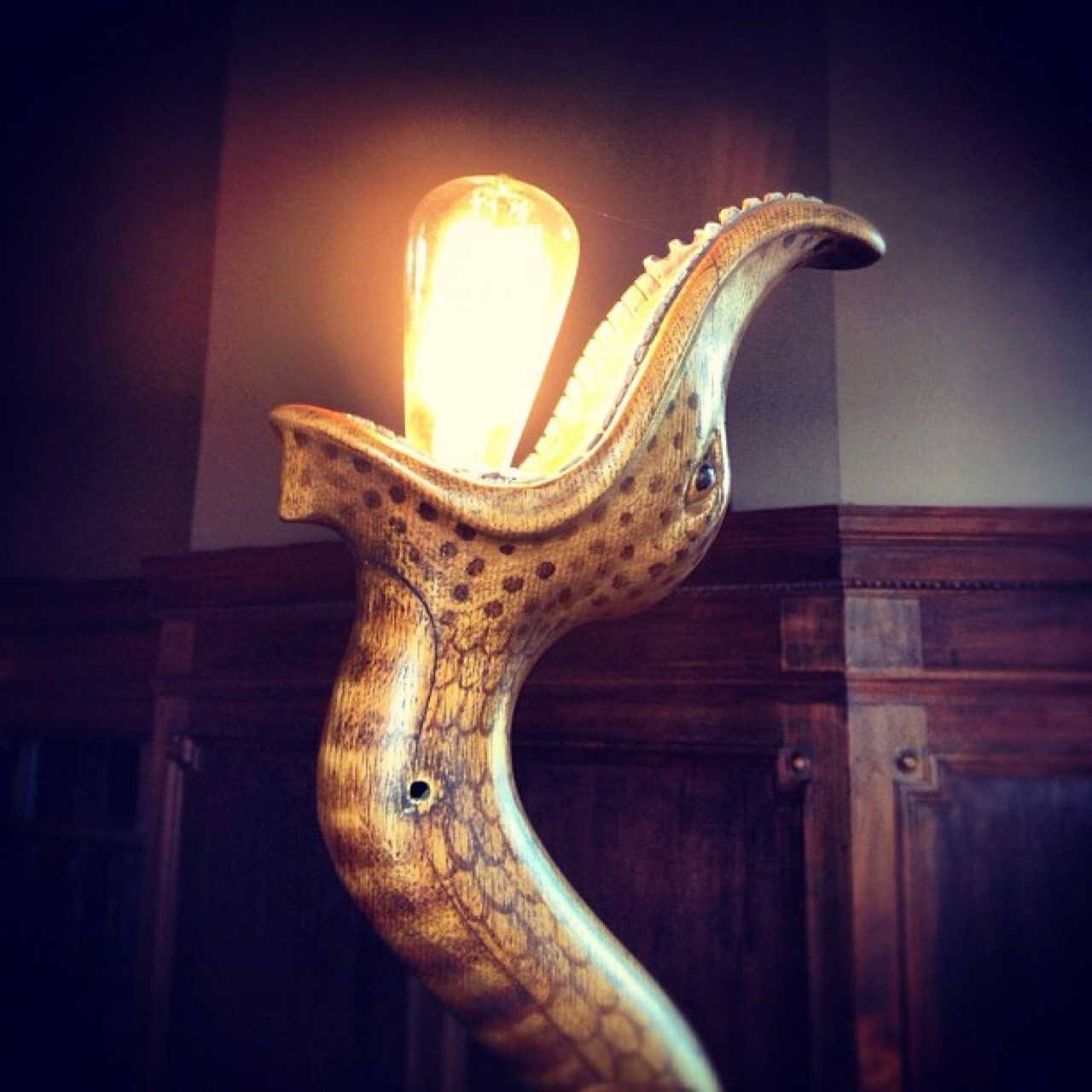 Carved serpent lamp cradling an Edison bulb