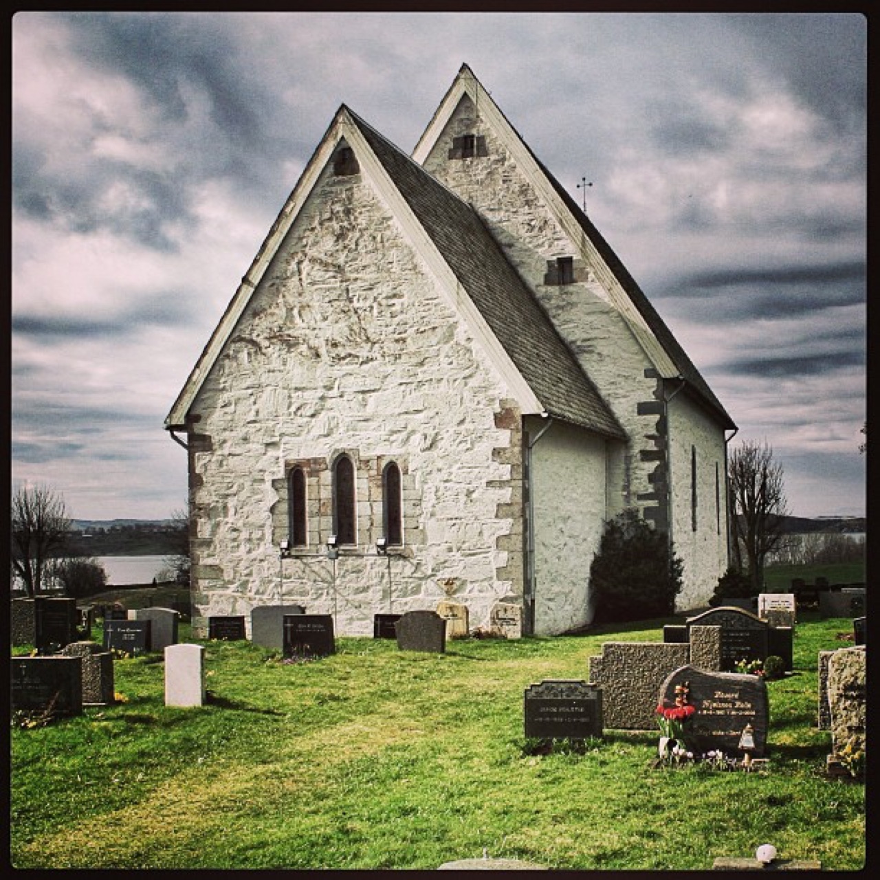 Stone church and churchyard under heavy clouds