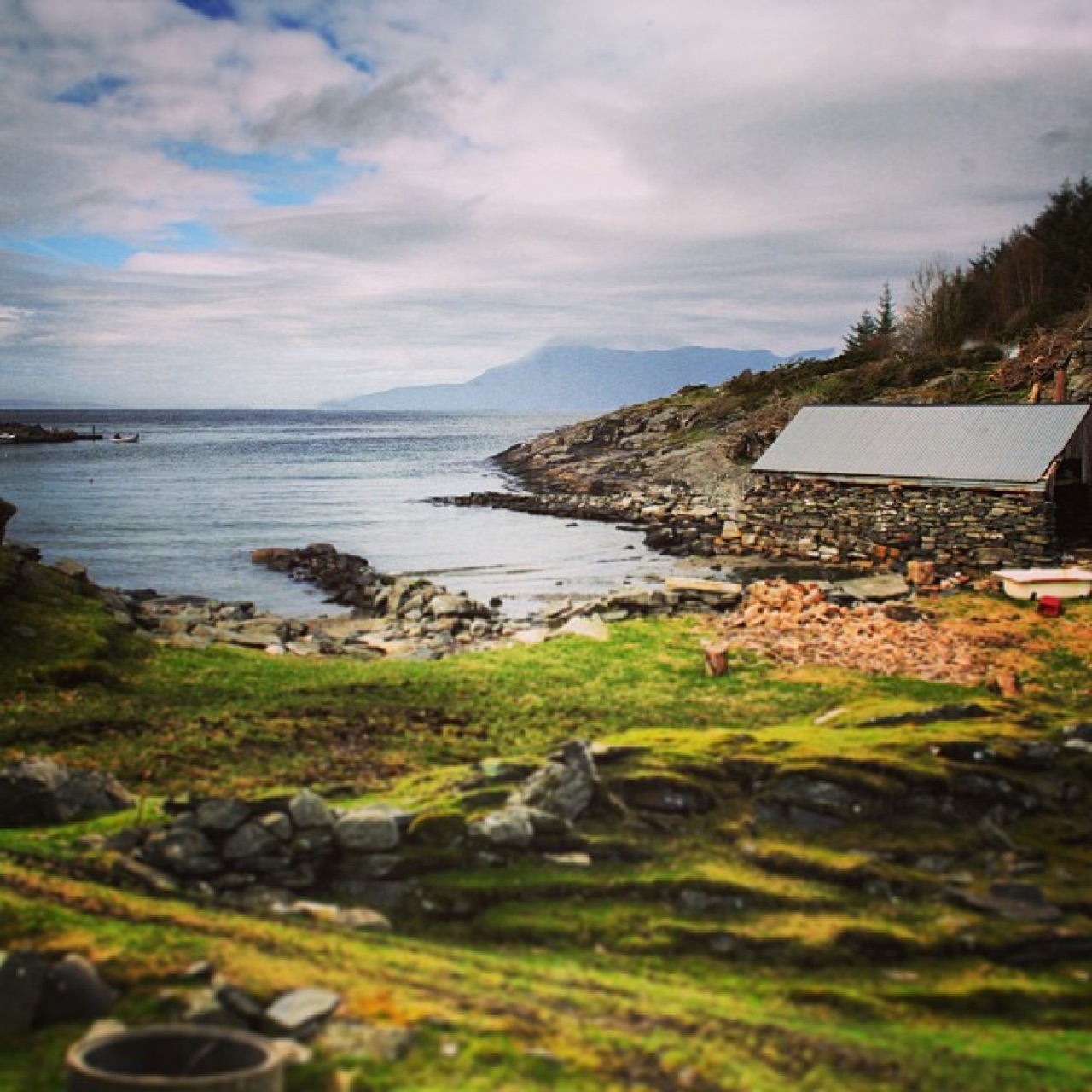 A old, stone boathouse sitting in a craggy Norway harbor in Spring.