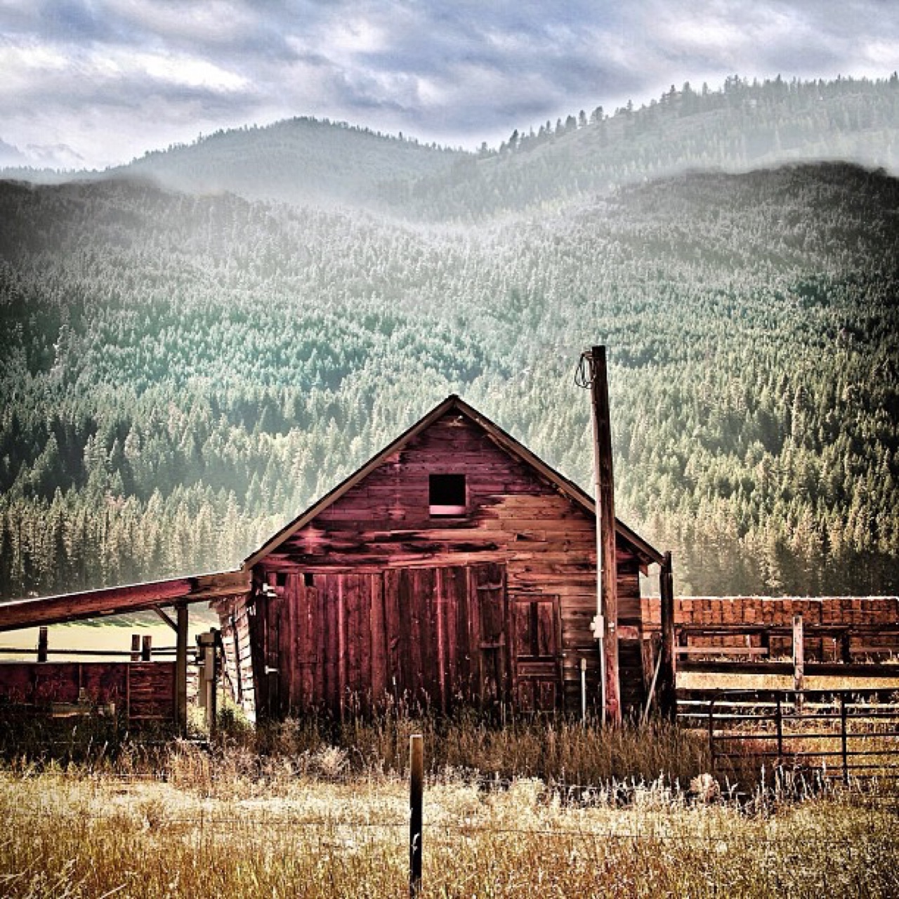 Weathered red barn under misty ridges