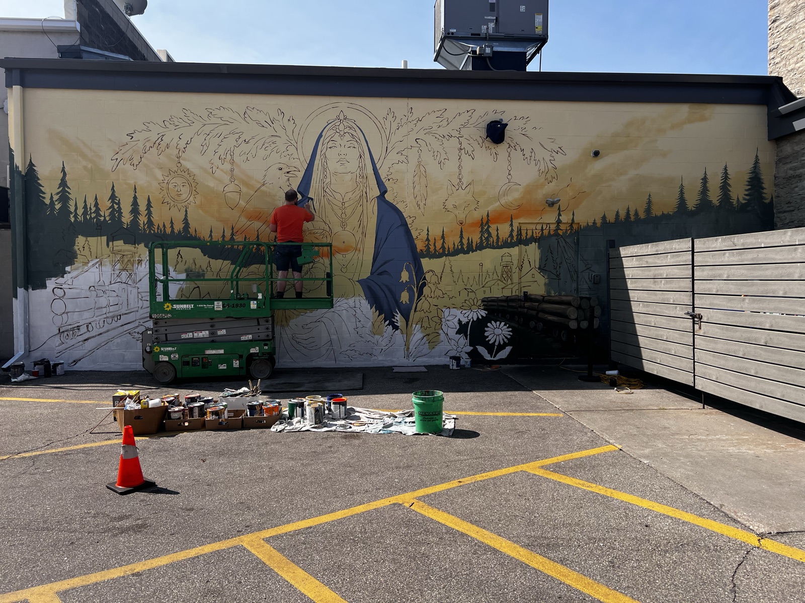 The mural mid-paint, the Madonna's blue robe being blocked in while an artist in an orange shirt works from a lift
