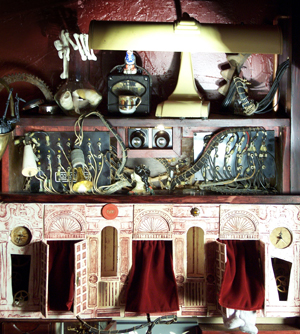 The two registers: the dark cabinet of instruments rising straight out of the painted dollhouse arcade.