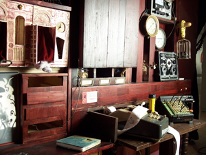 The cabinet wall, the painted dollhouse arcade at left, an adding machine and birdcage among the compartments.