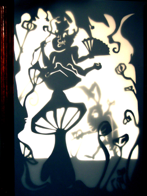The backlit shadow theater: a fan-bearing figure on a mushroom, a rabbit off to one side, hand-cut from black paper.